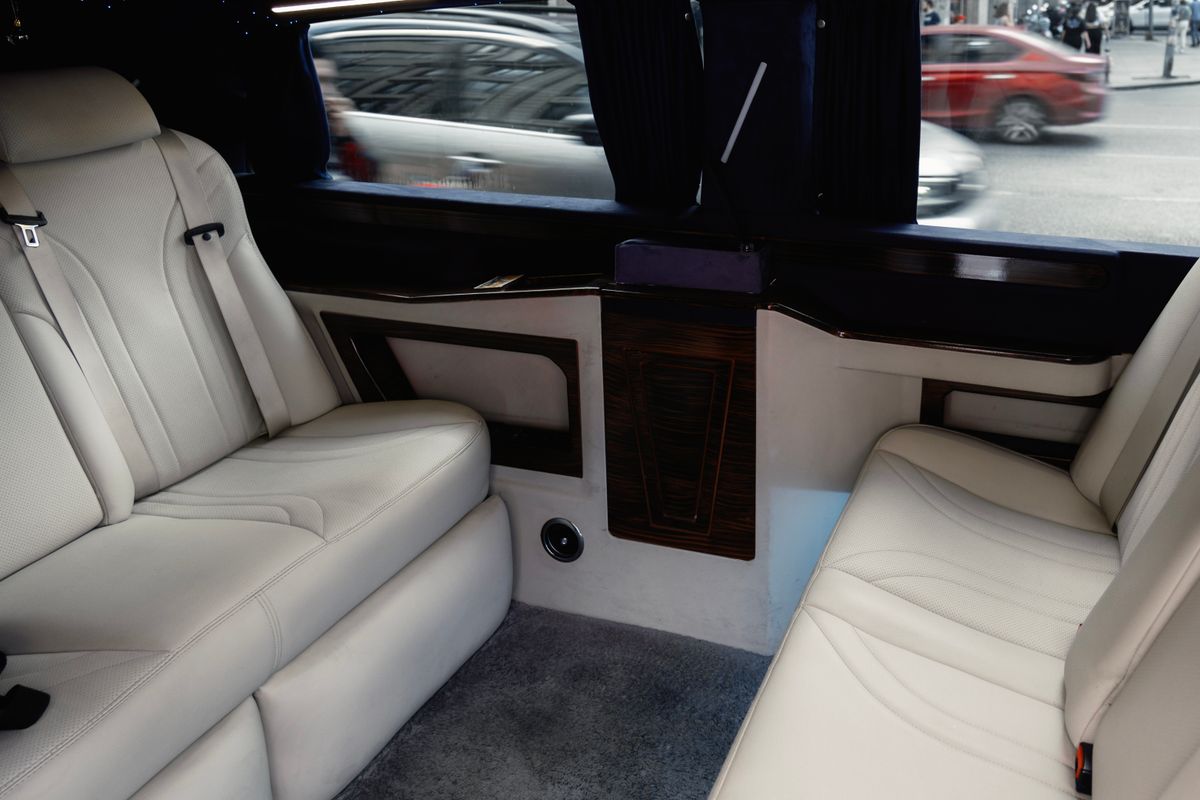 The cream leather rear cabin of a limousine with wood trim and curtains